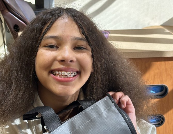 Smiling teen girl with braces holding a Lynnwood Orthodontics bag